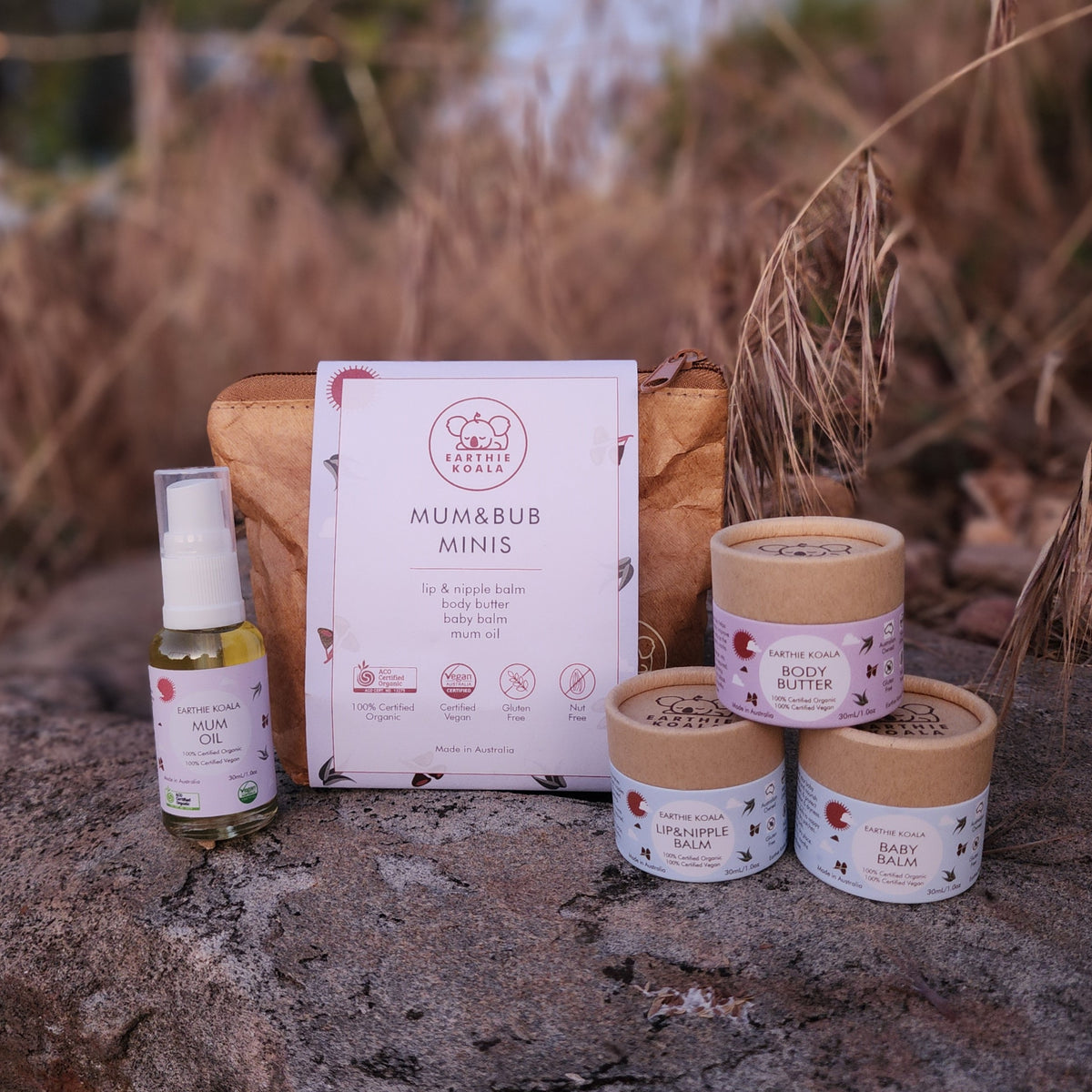 Mum and Bub Minis Set with Body Butter, Baby Balm, Mum Oil, and Lip &amp; Nipple Balm on a stone surface with blurred dried grass, organic skincare for mum and baby